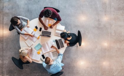 an aerial view of five people sitting at a table with laptops and open books